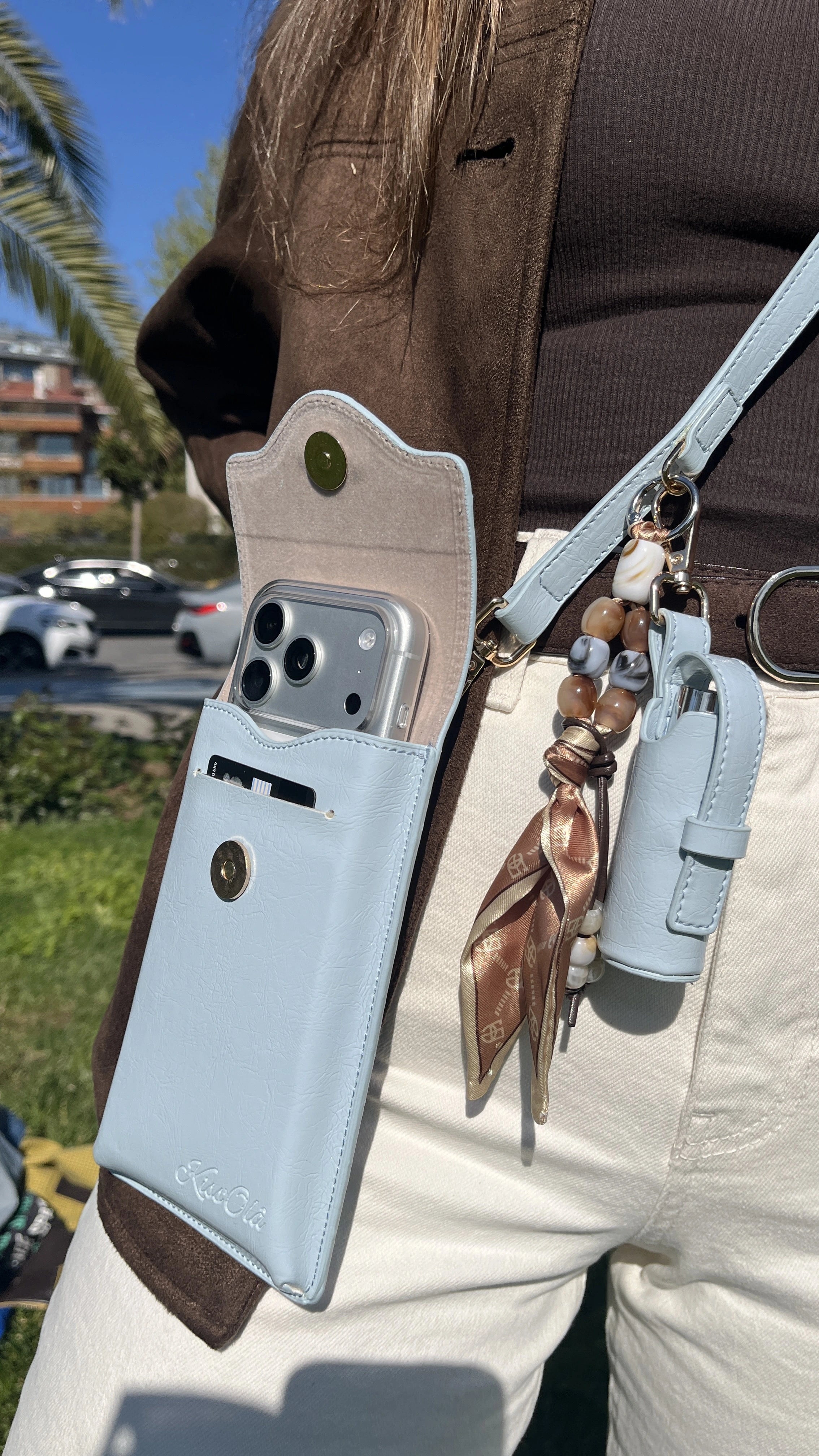 Bebek mavisi Kiss'Olâ Venice rujluk charmlı askılı telefon çantası, beyaz pantolon ve bohem charm ile yaz stili